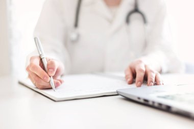 bir sabahlık bir stetoskop ile doktor bir masada oturur ve bir dizüstü bilgisayarda çalışır. Medecine, tanılama ve modern teknolojiler
