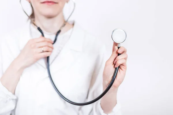 Jovem sorridente mulher morena médico em óculos e casaco branco médico, trabalhando estetoscópio close-up em um fundo branco — Fotografia de Stock