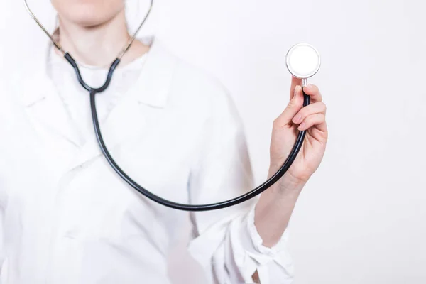 Jovem sorridente mulher morena médico em óculos e casaco branco médico, trabalhando estetoscópio close-up em um fundo branco — Fotografia de Stock