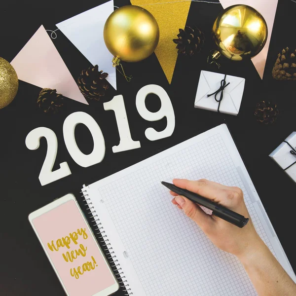 Happy New Years layout. numbers 2019 notepad and free space for text. Christmas decorations, Christmas toys, gifts, gold stars. Goals for the new year. mock up mobile phone on black background