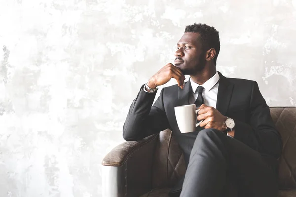 Homem afro-americano atraente em um terno de negócios em um interior elegante. empresário e líder da empresa. homem bebe café da manhã antes do trabalho por vivacidade — Fotografia de Stock