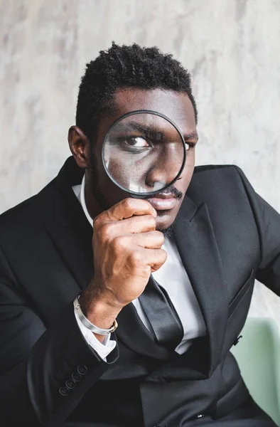 Enlarged eye of African American tax inspector looking through magnifying glass, inspecting offshore company financial papers, documents and reports. — Stock Photo, Image