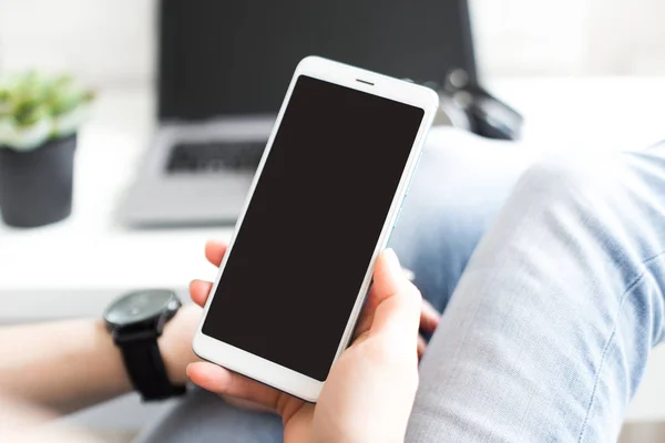 Imagen burlona de las manos de las mujeres sosteniendo el teléfono móvil blanco con pantalla en blanco en el muslo en la oficina — Foto de Stock