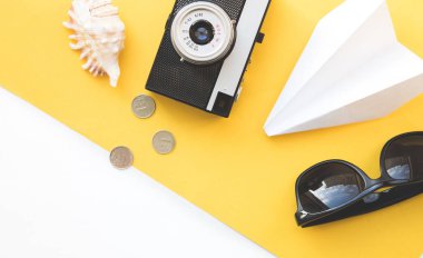 Flatlay seyahat aksesuarları metin için boş alan sarı zemin üzerine. Gözlük, kağıt uçak, eski fotoğraf makinesi, kabuk ve paralar, Top görüntülemek seyahat ya da tatil kavramı. Yaz arka plan.