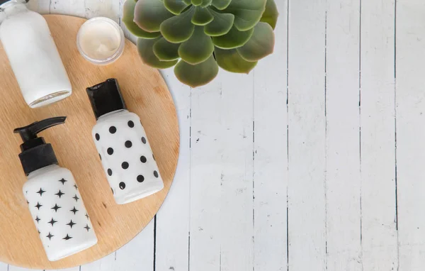 Beauty flat lay with cosmetic bottles, jar of face cream, succulent leaves and saw cut wood. Top view, minimalism, flatlay.