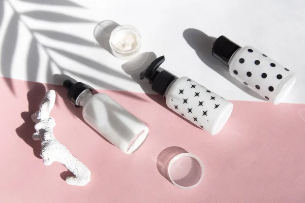 Beauty flat lay with spa cosmetic bottles, jar of face cream, tropical palm leaves and saw cut wood. Top view, minimalism, pink background flatlay