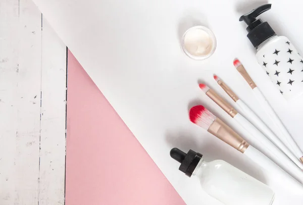 Beauty flat lay with spa cosmetic bottles, makeup brushes, jar of cream, tropical palm leaves and saw cut wood. Top view, minimalism, pink background flatlay