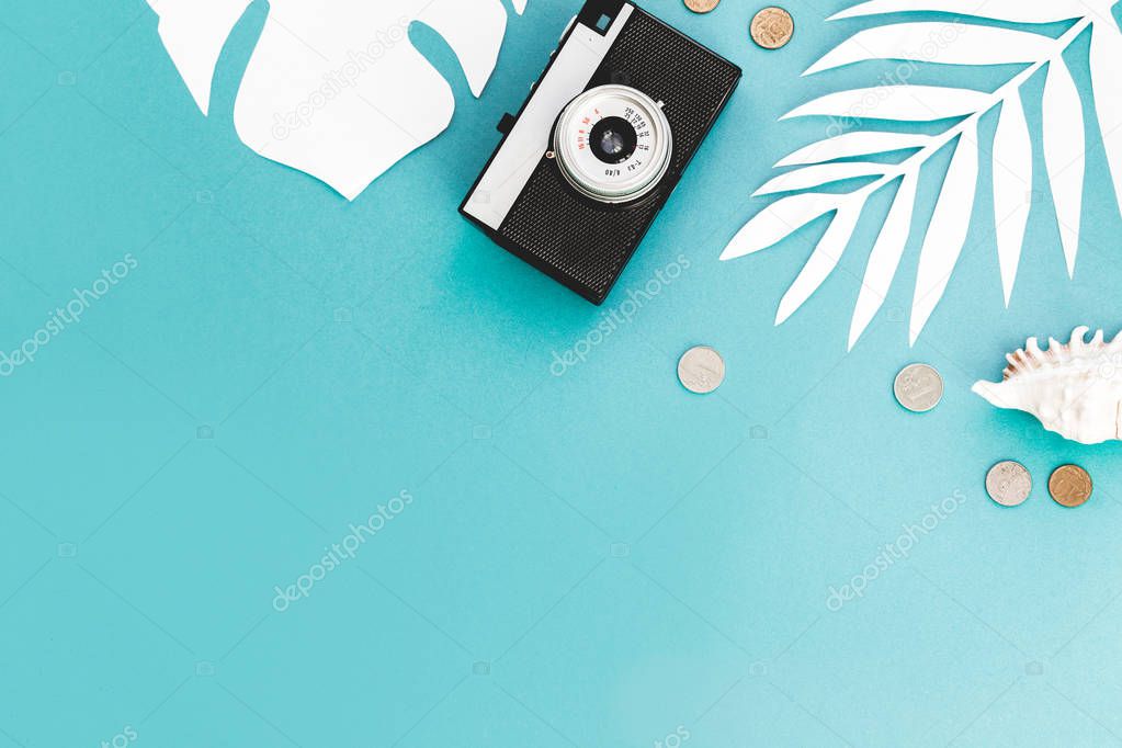 Flatlay traveler accessories on blue background with palm leaf, coin, shell, old camera and sunglasses. Top view travel or vacation concept and Summer background