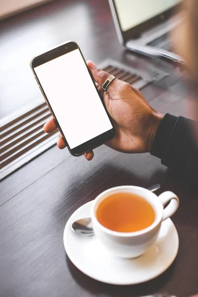 Hombre afroamericano sentado en un café, bebiendo café y trabajando detrás de un teléfono móvil. Mock up pantalla — Foto de Stock