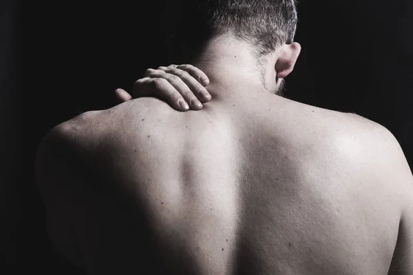 Egy férfi fájdalom a hát és a nyak. Közelről gazdaság a nyak a sötét háttér. — Stock Fotó