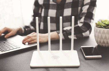 Kız ofiste beyaz Wi Fi yönlendirici yakın elinde telefon ile Laptop çalışır. Çok