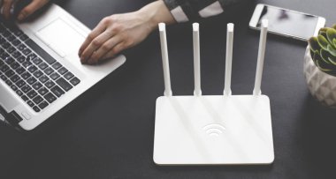 Kız ofiste beyaz Wi Fi yönlendirici yakın elinde telefon ile Laptop çalışır. Çok