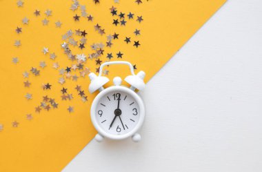 Beyaz masa saati, sarı arka planda alarm, üst görünüm. Günaydın. Minimalizm, düzlük