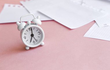 Beyaz masa saati, parlak arka planda çalar saat, üst görünüm. Ofiste iş yerinde mola. Kağıt, düzlük