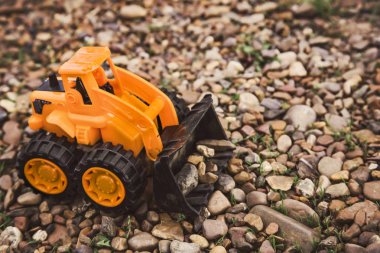 bir kova ile oyuncak turuncu traktör kum bir dağ üzerinde taş taşır