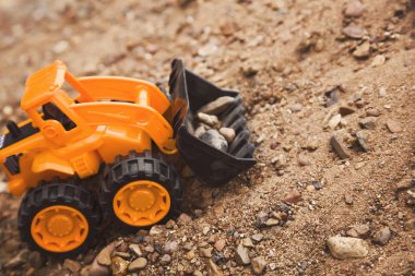 bir kova ile oyuncak turuncu traktör kum bir dağ üzerinde taş taşır