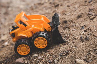 bir kova ile oyuncak turuncu traktör kum bir dağ üzerinde taş taşır