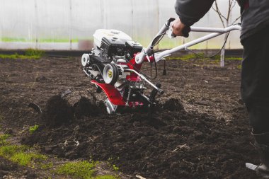 Bir adam bir el traktörü yetiştirici ile bahçede arazi sürme bir çiftçidir. Tohum ekimi için tarlanın sabanlanması konusunda tarımsal çalışmalar