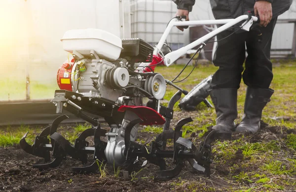 Um homem é um agricultor que lavra a terra no jardim com um cultivador de tratores manuais. Trabalhos agrícolas na lavoura do campo para sementeira de sementes — Fotografia de Stock