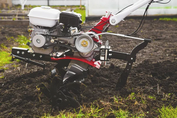 A man is a farmer plowing the land in the garden with a hand tractor cultivator. Agricultural work on plowing the field for sowing seeds — Stock Photo, Image