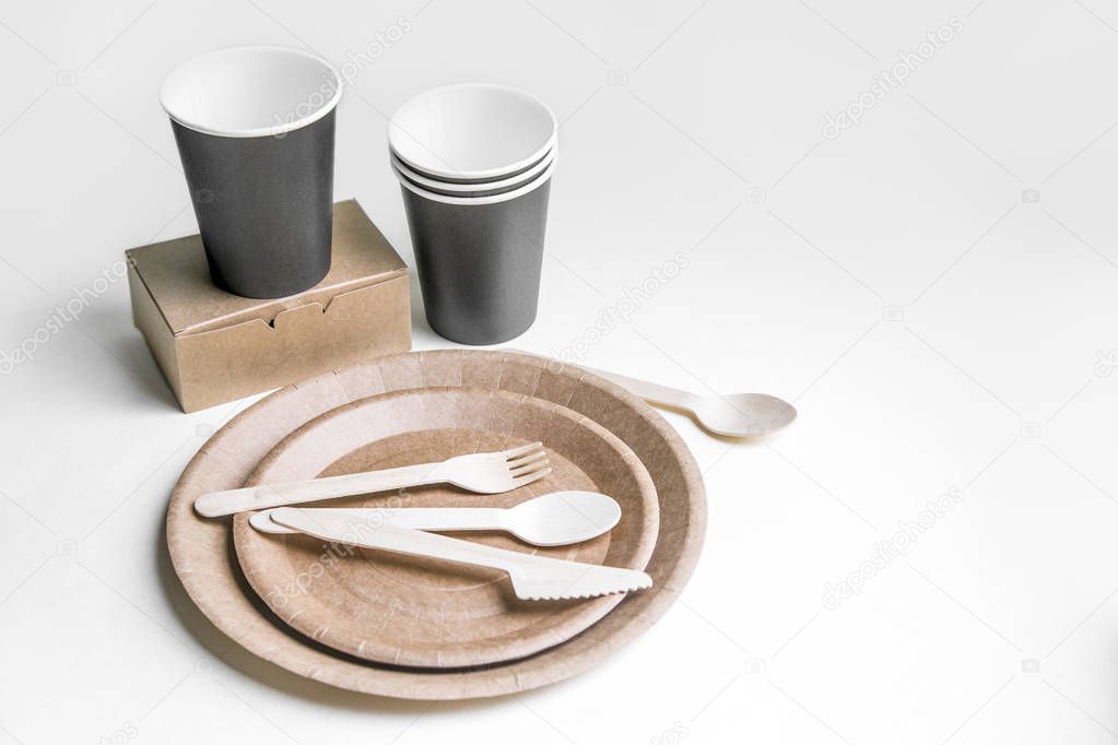eco friendly disposable dishes made paper on white marble background. Draped spoons, fork, knives, plate with paper cups. recycling concept