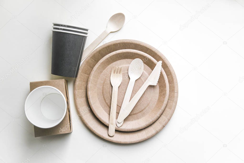 eco friendly disposable dishes made paper on white marble background. Draped spoons, fork, knives, plate with paper cups. recycling concept