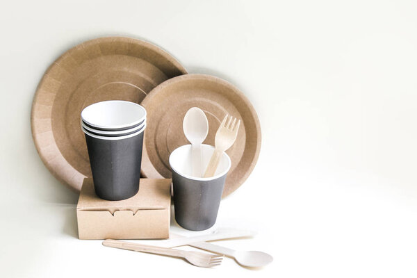 eco friendly disposable dishes made paper on white marble background. Draped spoons, fork, knives, plate with paper cups. recycling concept