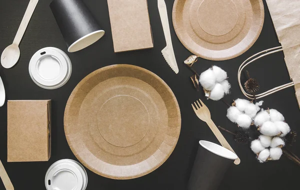 Екологічно чистий одноразовий посуд з паперу на чорному тлі. Загорнуті ложки, виделка, ножі, тарілка з паперовими чашками. концепція переробки — стокове фото