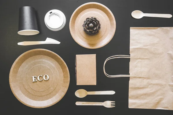 Eco friendly disposable dishes made paper on black background. Draped spoons, fork, knives, plate with paper cups. recycling concept — Stock Photo, Image