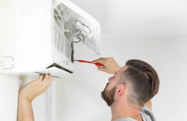 Erkek teknisyen içeride klimayı temizliyor. Klimayı temizleyen teknisyen servisi.