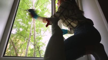 Mavi eldivenli bir kadın, evinde bez ve temizleyici sprey ile pencereyi temizliyor. temizlik servisi
