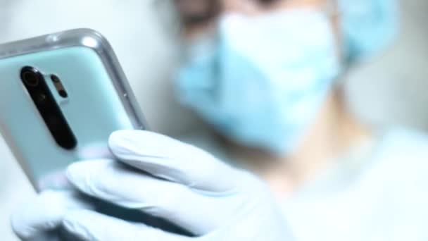 Enfermeira com máscara durante a pandemia de Coronavirus, e em óculos de segurança, luvas. Close up, mulher falando em um smartphone — Vídeo de Stock