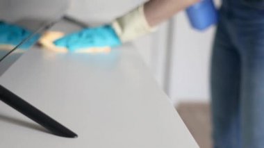 Lastik eldivenli bir kadın şifoniyerin üzerindeki bir bezle tozu siler. Ev Temizlik Servisi.
