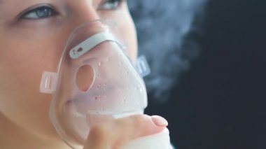 Boğazı ağrıyan hasta kadın yüzünde maskeyle solunum yapıyor. Hasta hasta kendini nebulizör ile iyileştiriyor.