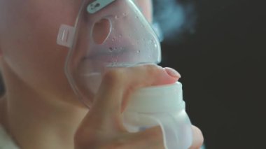 Boğazı ağrıyan hasta kadın yüzünde maskeyle solunum yapıyor. Hasta hasta kendini nebulizör ile iyileştiriyor.