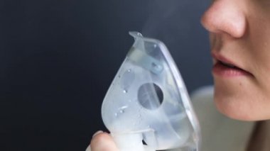Boğazı ağrıyan hasta kadın yüzünde maskeyle solunum yapıyor. Hasta hasta kendini nebulizör ile iyileştiriyor.