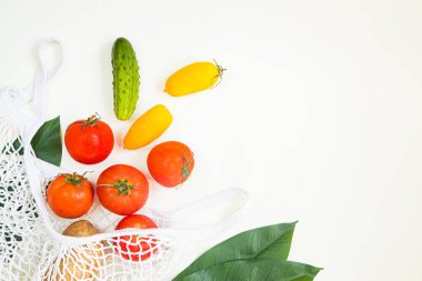 Domateslerden, salatalıklardan ve beyaz arka planda yapraklardan oluşan yaratıcı doğal düzen. Düz yatıyordu. eko çanta.