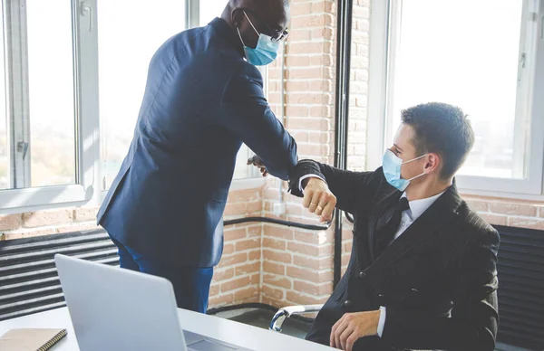 Dwóch biznesmenów w maskach ochronnych na twarz witających uderzające łokcie w miejscu pracy, męscy współpracownicy w maskach na twarz chronią przed COVID-19 w biurze, koncepcja opieki zdrowotnej — Zdjęcie stockowe