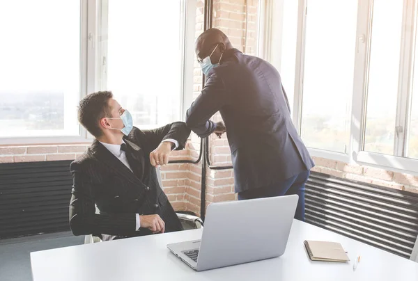 Dwóch biznesmenów w maskach ochronnych na twarz witających uderzające łokcie w miejscu pracy, męscy współpracownicy w maskach na twarz chronią przed COVID-19 w biurze, koncepcja opieki zdrowotnej — Zdjęcie stockowe