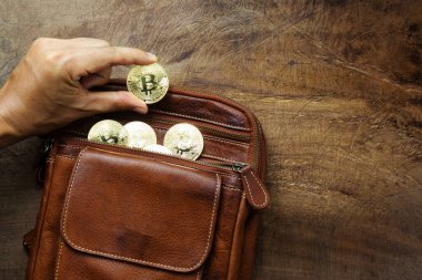Adamın eli bitcoin topluyor. Paralar ahşap masadaki kahverengi deri çantalarda çok parlak. İş ve ticaret için tasarım kavramı