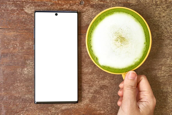 El masada bir cep telefonu ve yeşil çay bir bardak ile oynuyor         