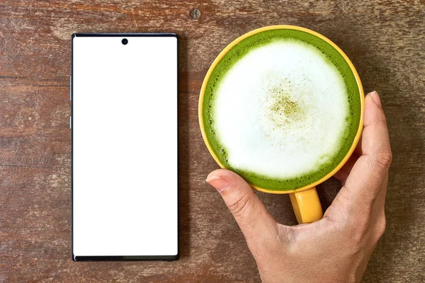 El masada bir cep telefonu ve yeşil çay bir bardak ile oynuyor         