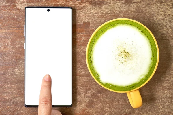 El masada bir cep telefonu ve yeşil çay bir bardak ile oynuyor         