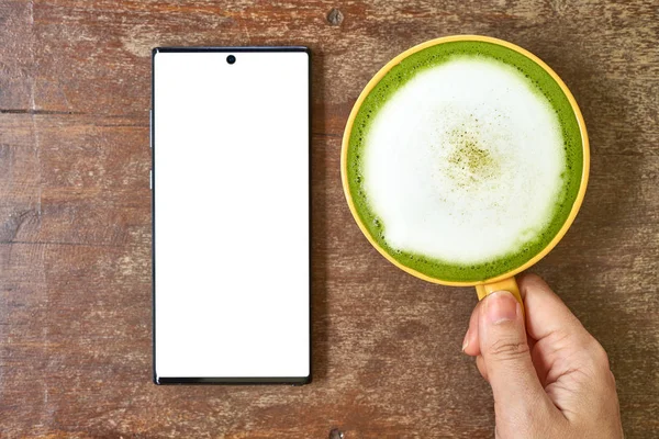 El masada bir cep telefonu ve yeşil çay bir bardak ile oynuyor         