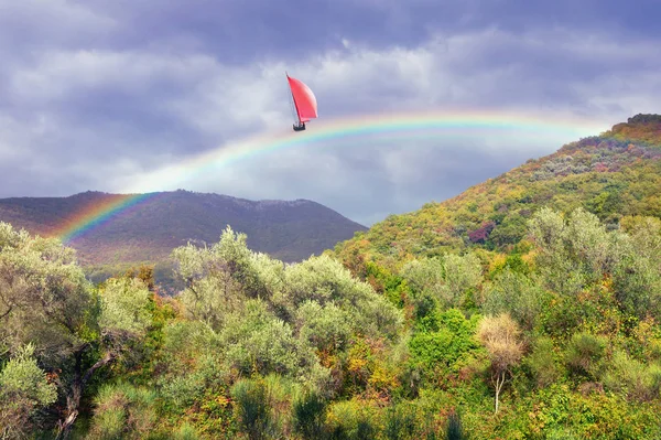Happy day. Sailboat sails along the rainbow between mountains.  Photo manipulation. Travel, dream, fantasy concept