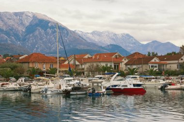 Bulutlu kış günü. Küçük marina Dağları'nın eteklerinde balıkçı tekneleri için. Karadağ, Kotor Körfezi. Tivat şehir ve Lovcen Dağları doruklarına Marina Kalimanj
