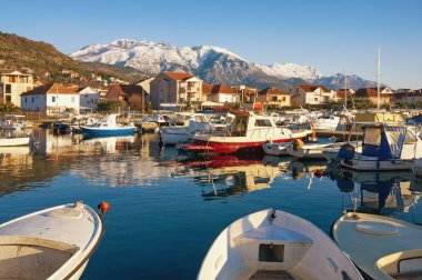 Güneşli kış günü. Karlı Dağları'nın eteklerinde Akdeniz şehirdeki Limanındaki balıkçı tekneleri. Karadağ, Kotor Körfezi. Marina Kalimanj Tivat şehir ve Lovcen Dağları'nın karla kaplı görünümünü
