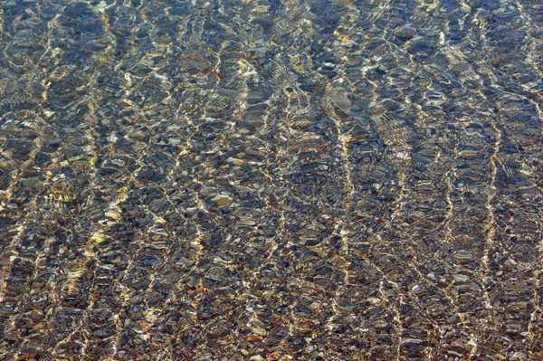 Płytkie wody na kamienistej plaży morza na spokojny słoneczny dzień, tekstura — Zdjęcie stockowe