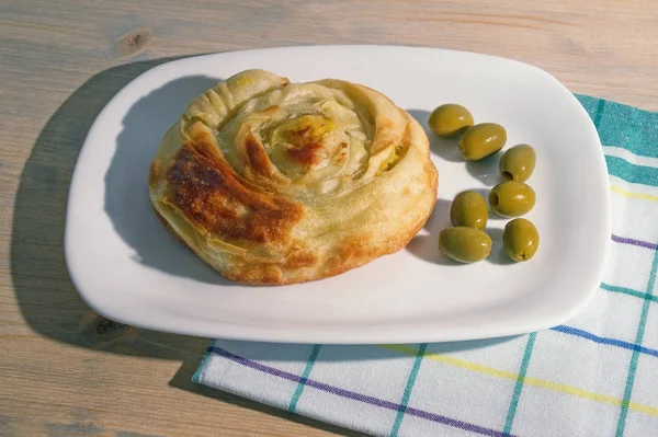 Cozinha balcânica. Burek - prato nacional popular, é bolo quente feito com massa folhada. Escritório redondo em uma placa branca, fundo rústico — Fotografia de Stock