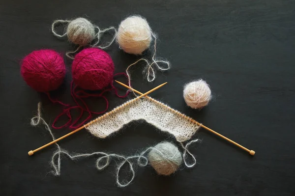 Balls of wool  and unfinished knitting on black background, flat lay. Free space for text — Stock Photo, Image